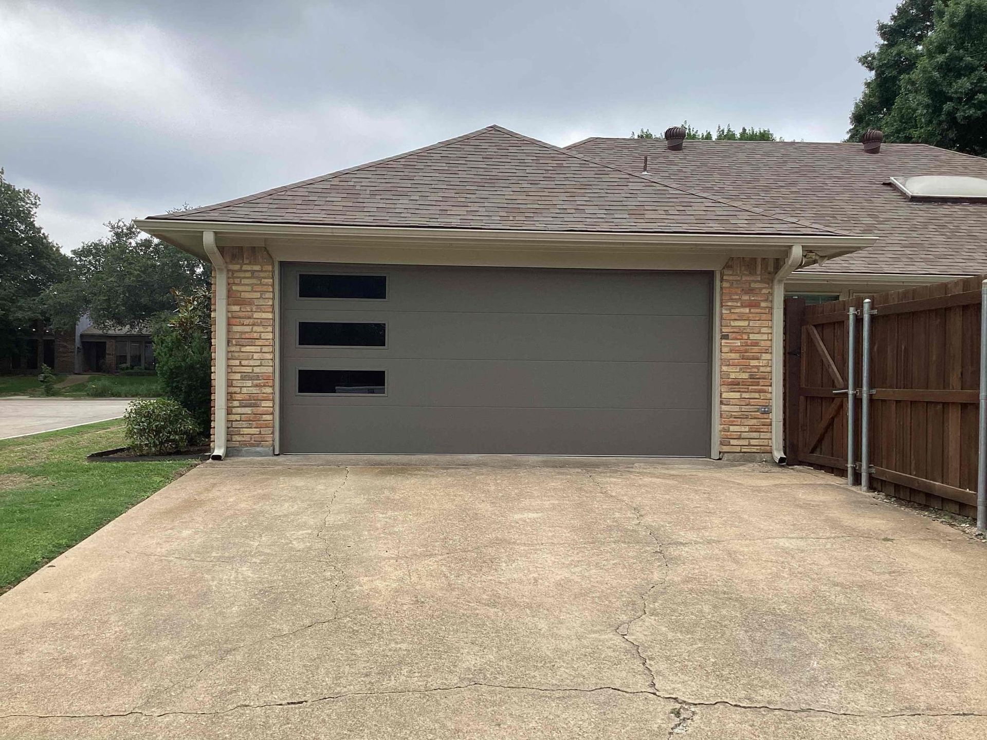 A brown garage door with three small, horizontal windows on the left, set in a stone-trimmed house with a concrete driveway.