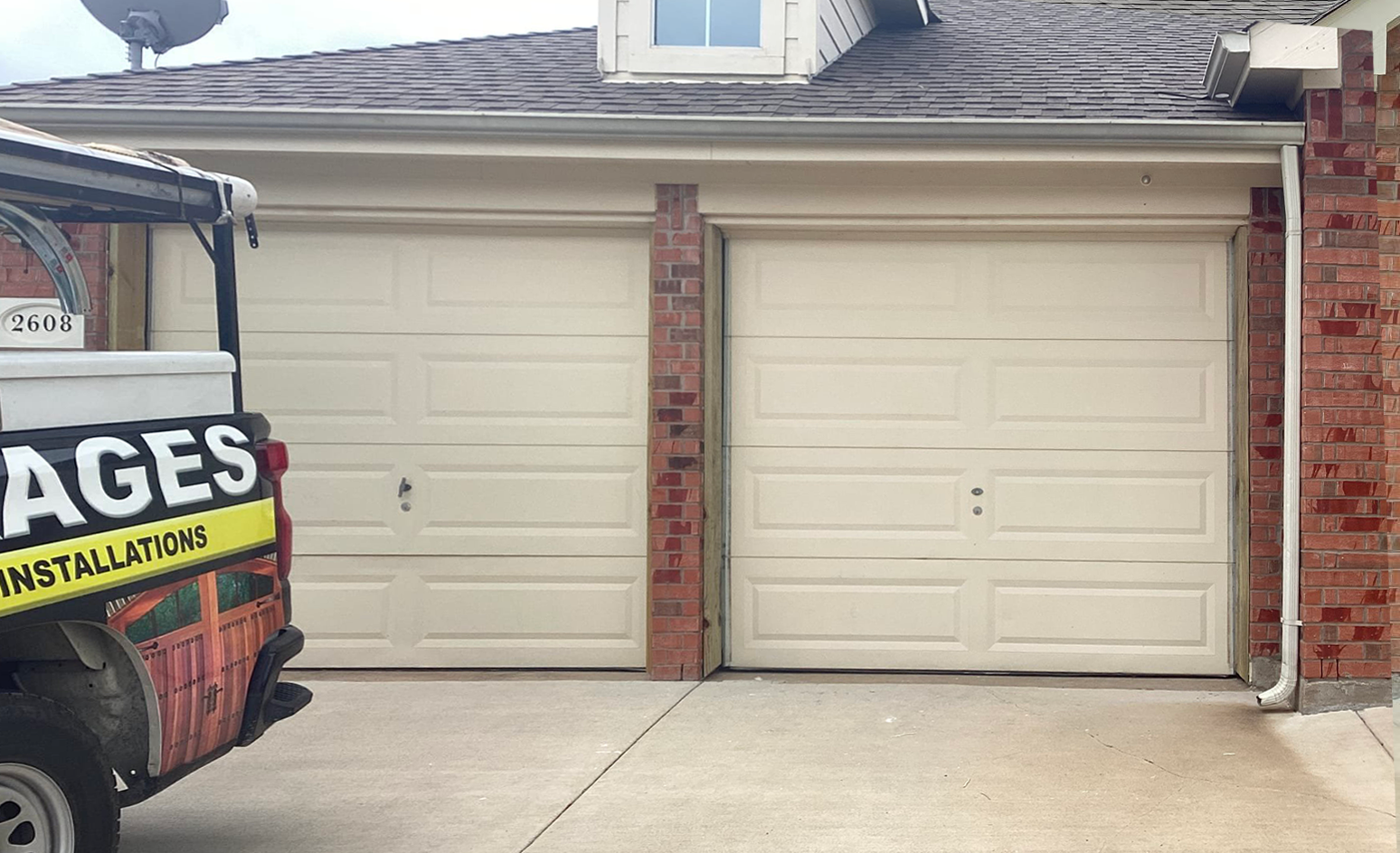 Two beige garage doors next to each other, with a brick pillar in between. A service vehicle is parked on the left.