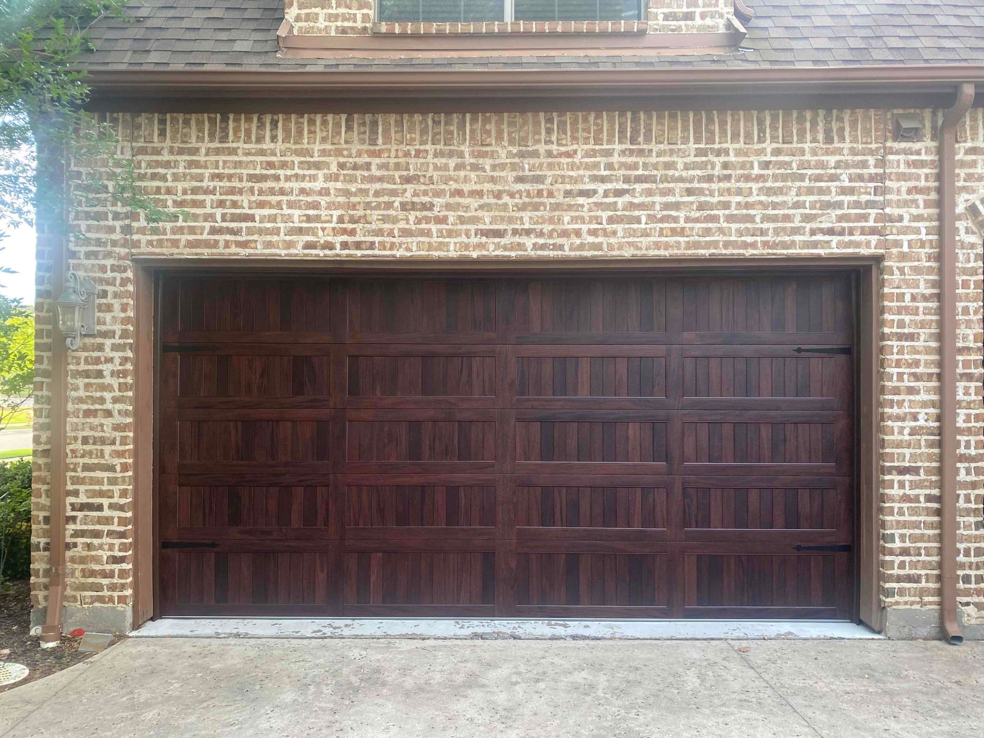 A dark wood-toned garage door with a paneled design on a brick residential building exterior.