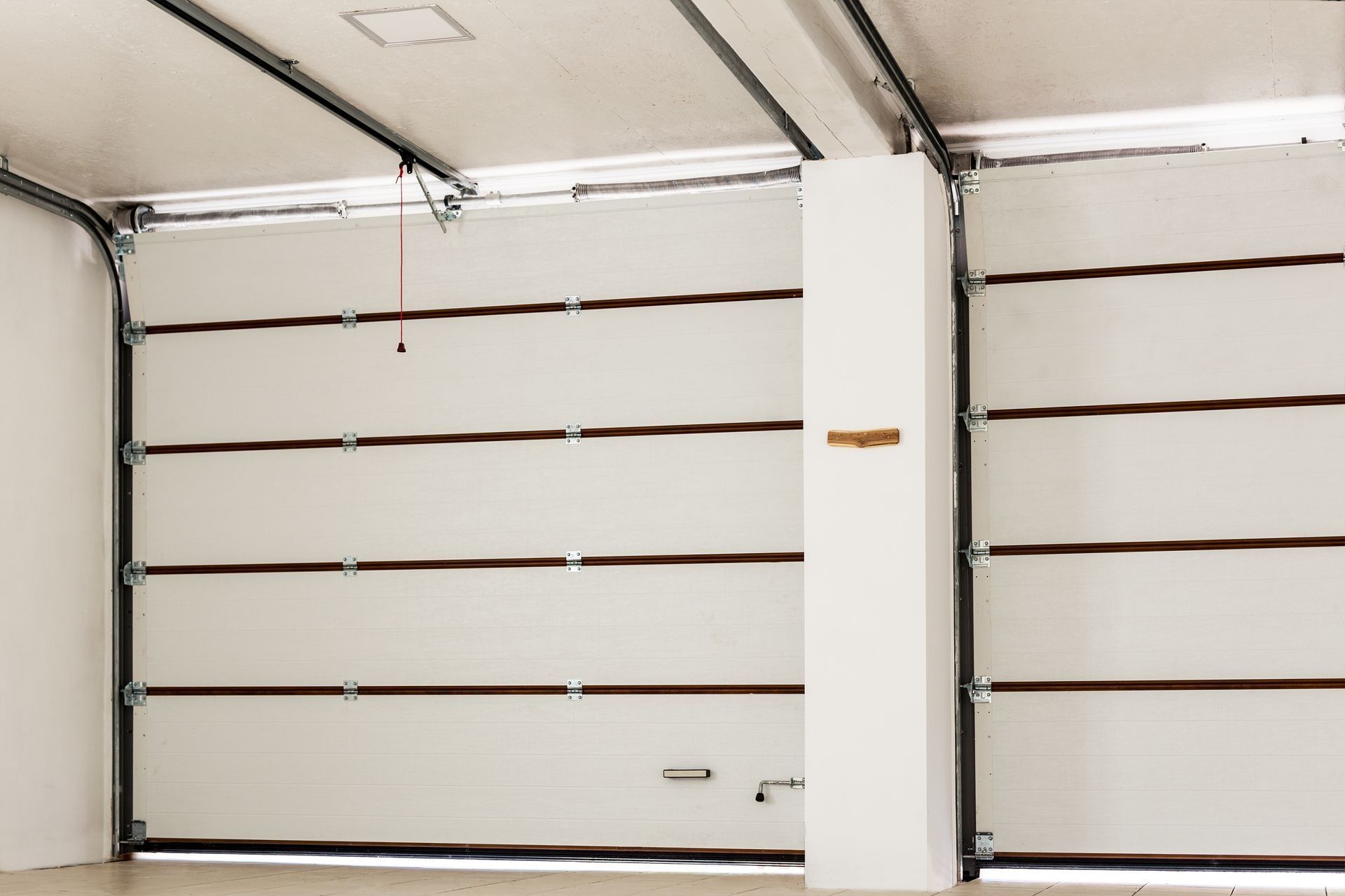 White garage doors, partially open, with horizontal panels and brown accents. Interior view with a support column.