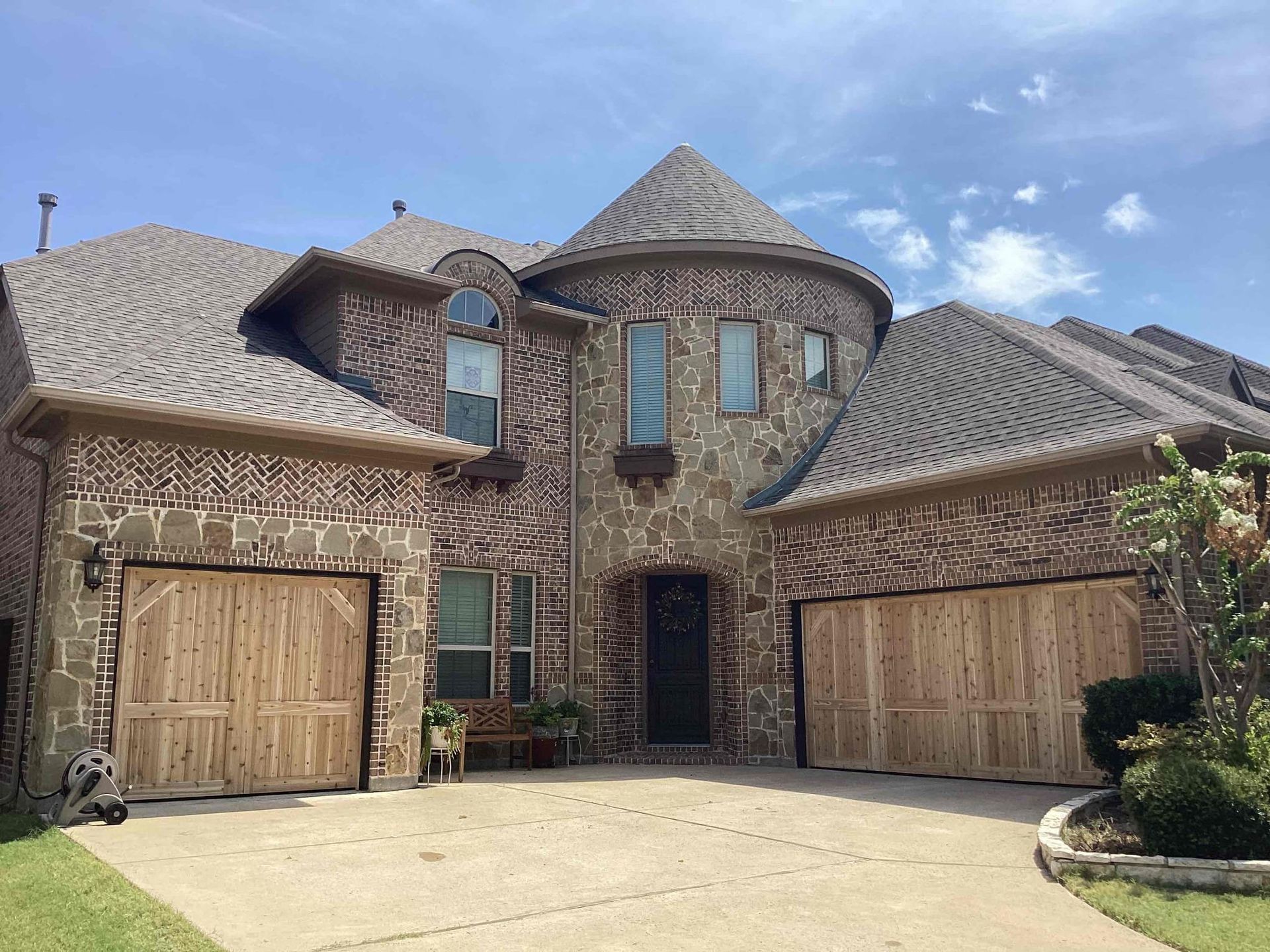 A two-story house with a brick exterior, a central turret, light wood garage doors, and a concrete driveway.