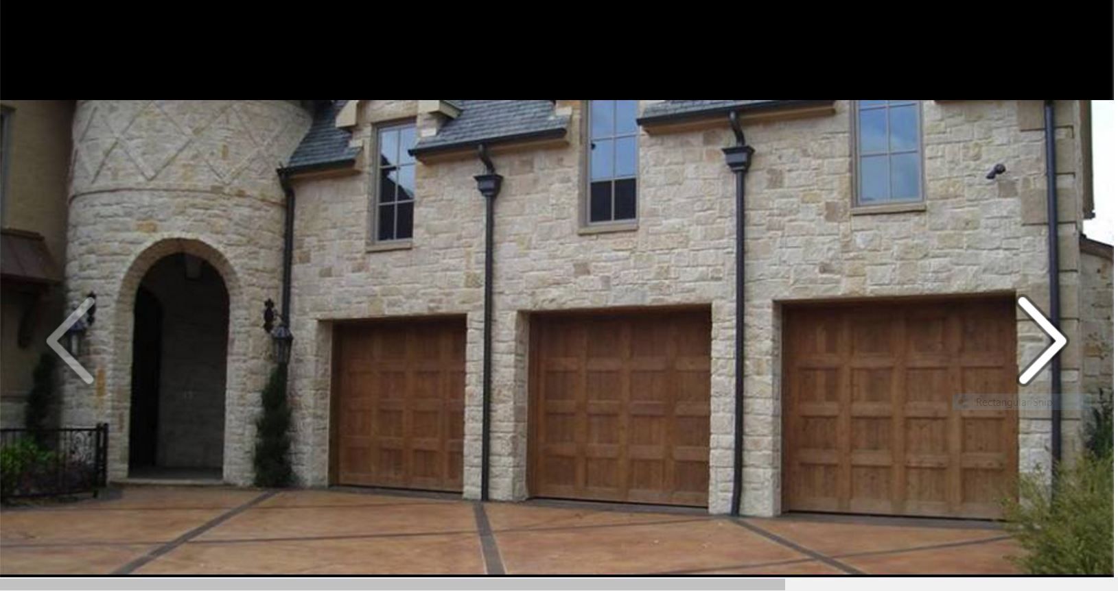 A stone-facade house with three wooden garage doors and an arched entryway.