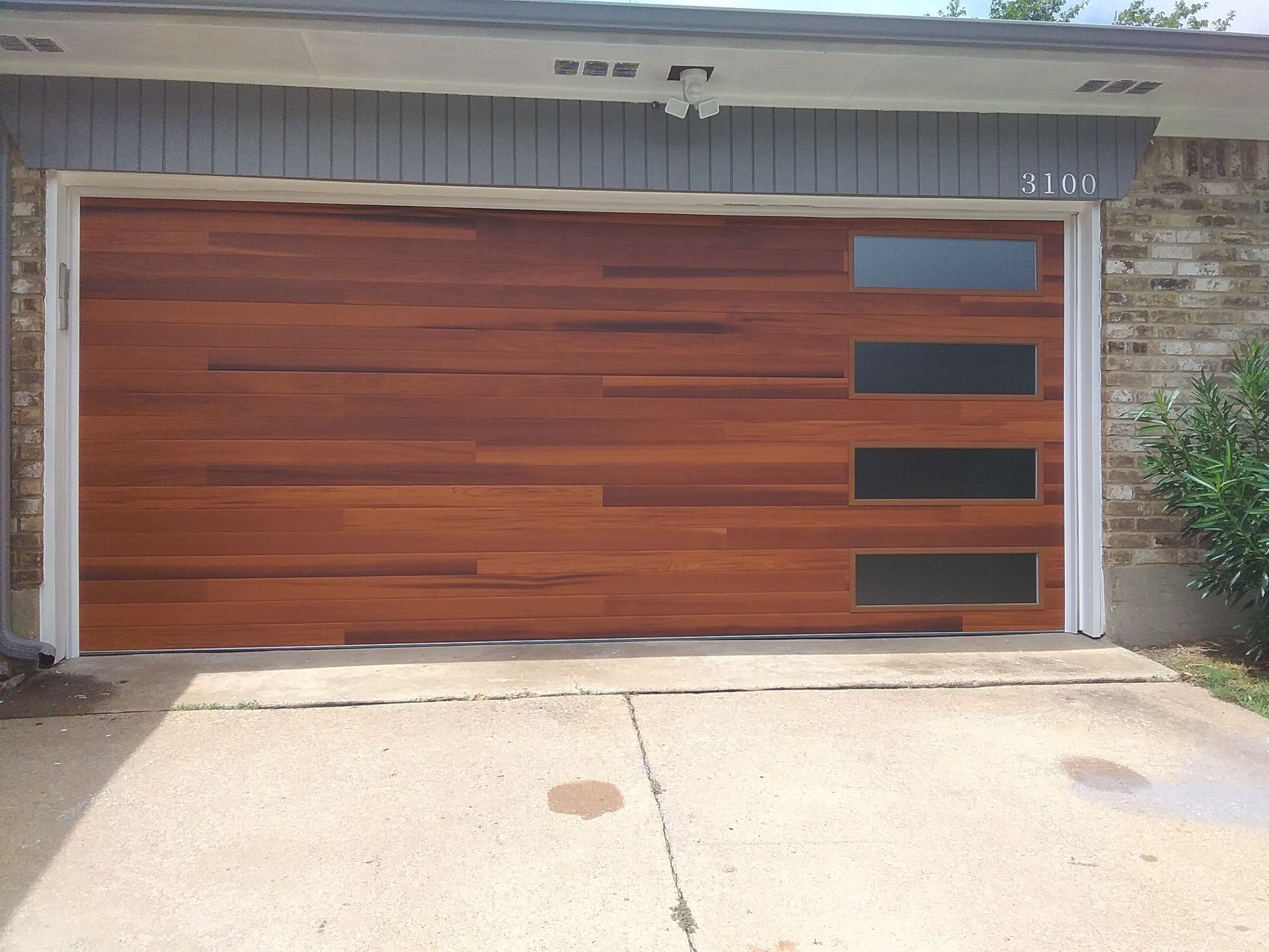 A modern wooden garage door with a row of four horizontal windows on the right side, mounted on a brick house.