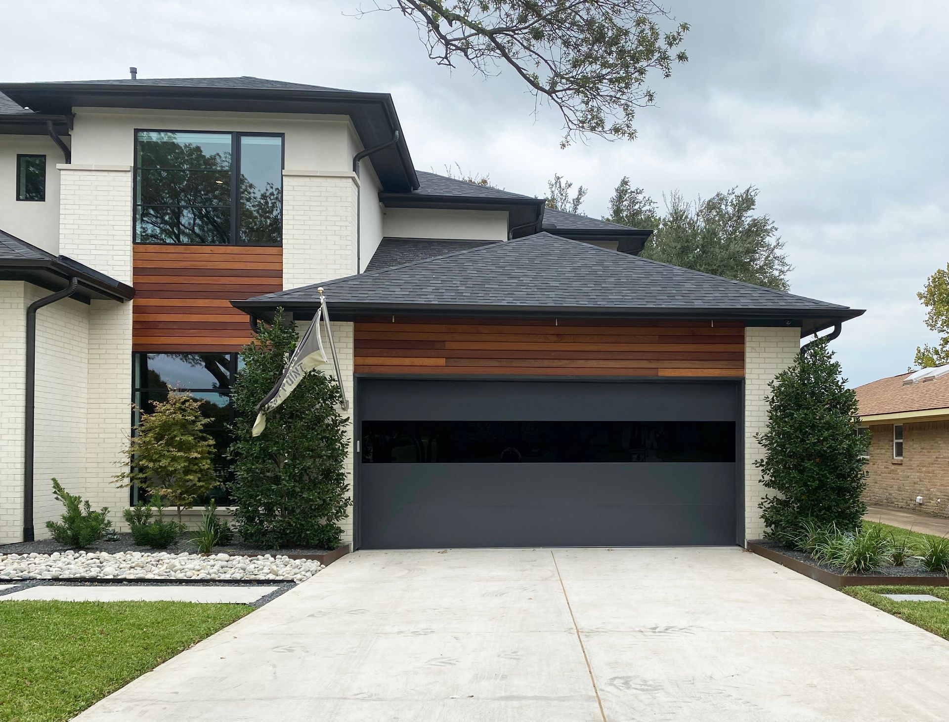 Modern two-story house with white stone, wood accents, a dark gray garage door, and a gray shingled roof.