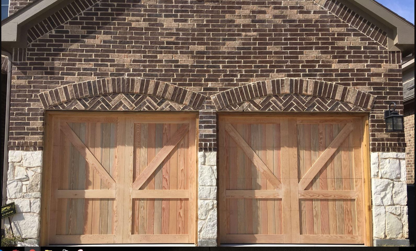 Two wooden garage doors with diagonal bracing under decorative arched brick lintels and a partial stone facade.