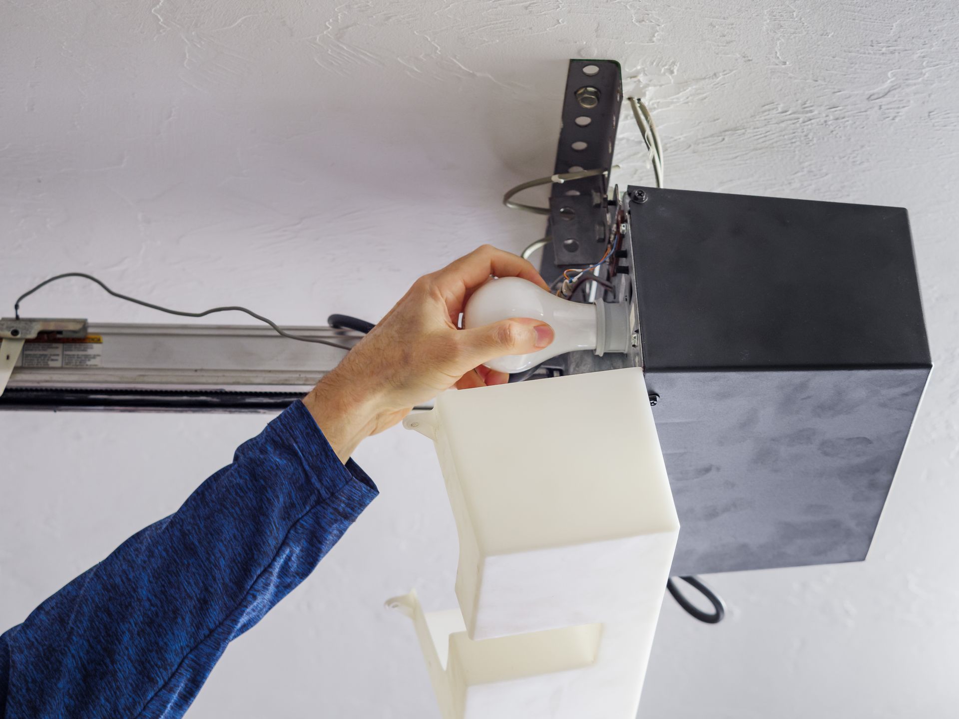 Hand replacing light bulb in garage door opener unit on ceiling. Hand replacing light bulb in garage door opener unit on ceiling.