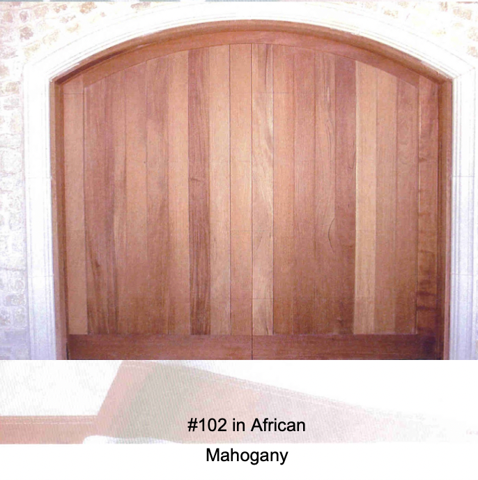 An arched wooden garage door made of African Mahogany with vertical panels, framed by a stone entryway.