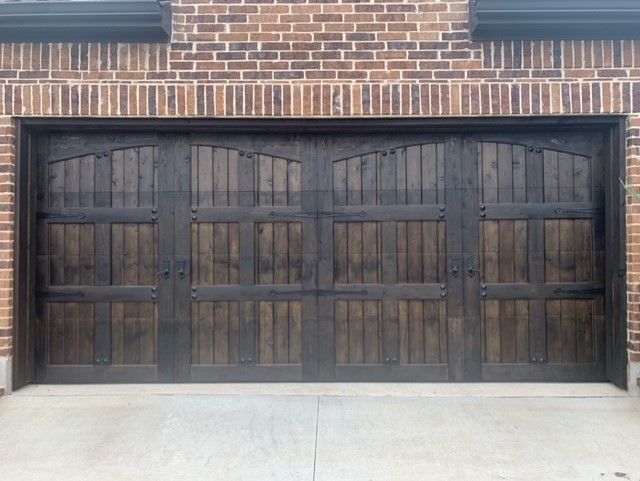 A large, dark-stained wooden garage door with a multi-panel design, set into a brick exterior wall.