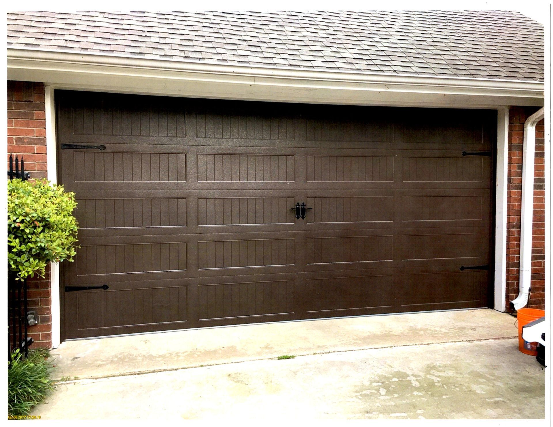 A closed, dark brown residential garage door with decorative black hinges and a center handle set in a brick exterior.
