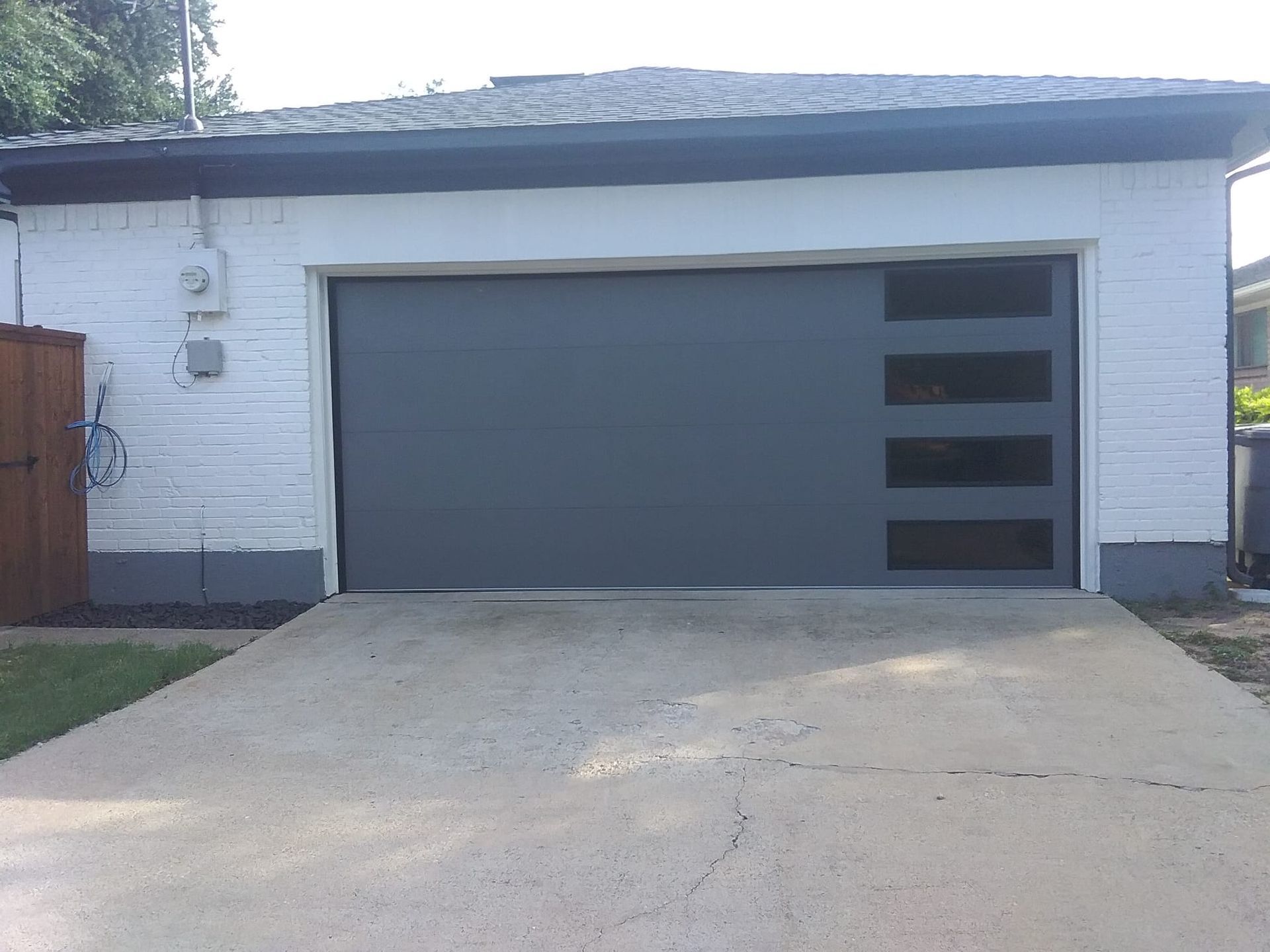White brick garage with a dark gray flat door featuring a vertical row of four narrow, rectangular windows on the right.