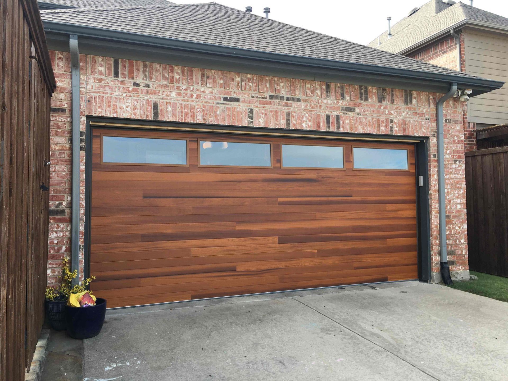 A wood-paneled garage door with horizontal planks and four rectangular windows set in a brick residential exterior.