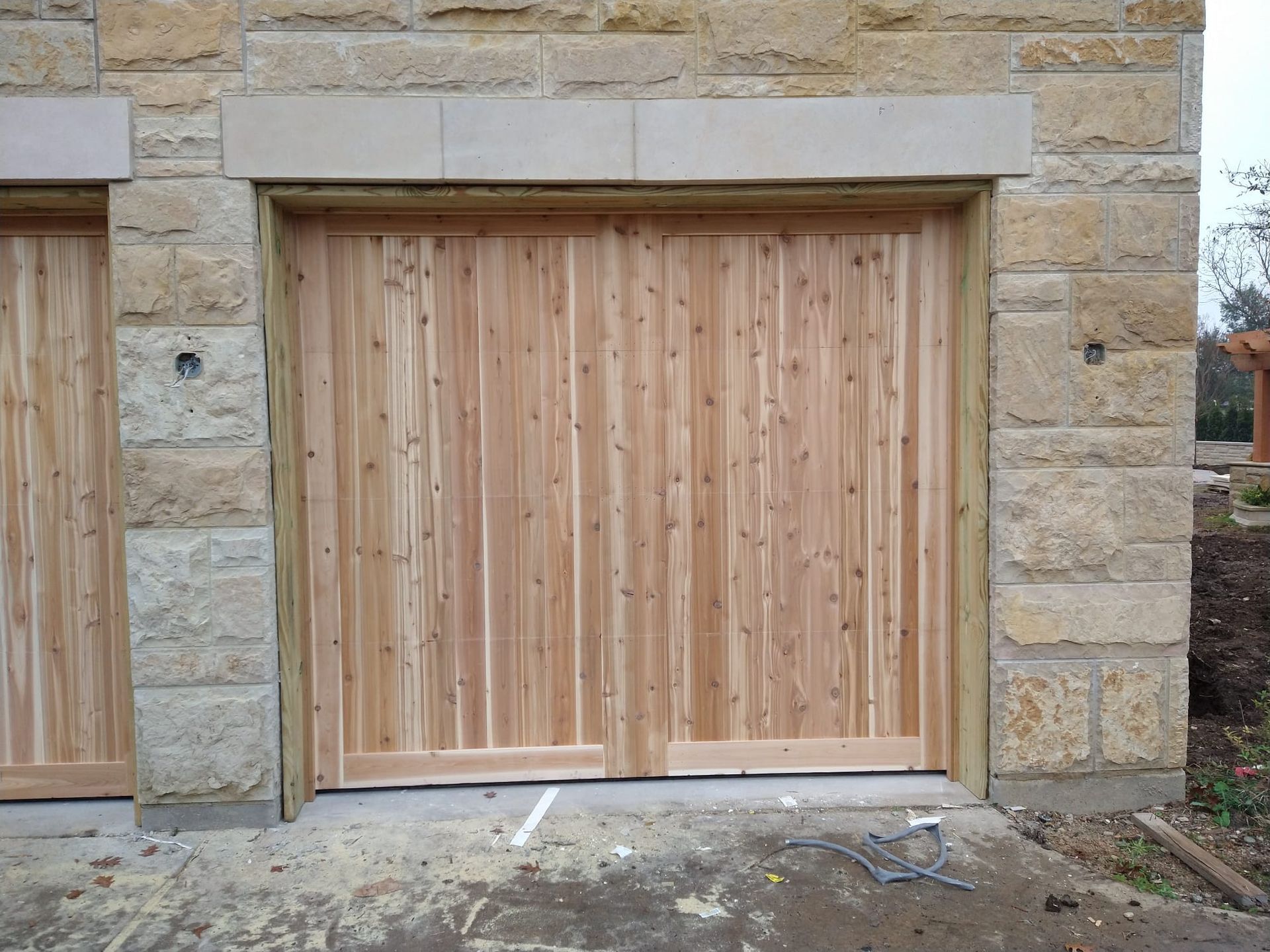 A newly installed wooden garage door with vertical slats set into a light-colored, rustic stone wall.