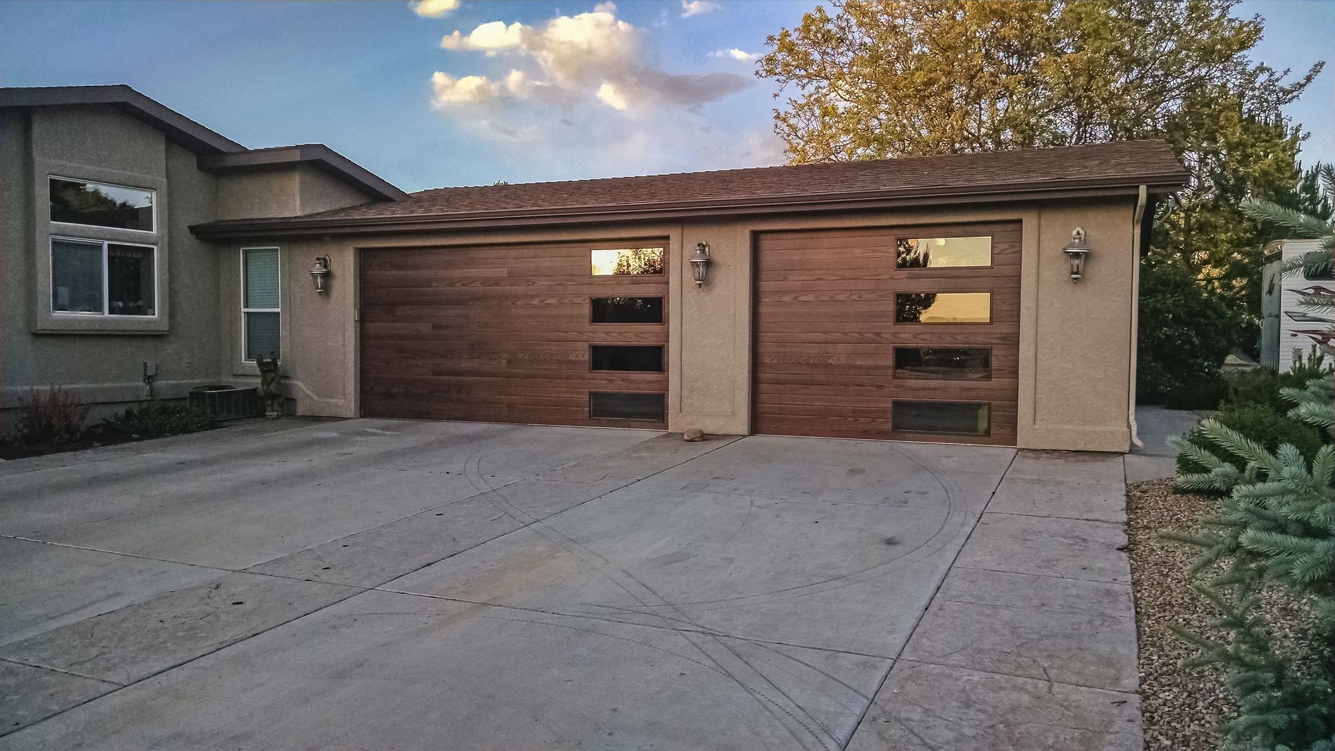 A suburban home exterior featuring two modern, dark wood-paneled garage doors with horizontal glass window inserts.