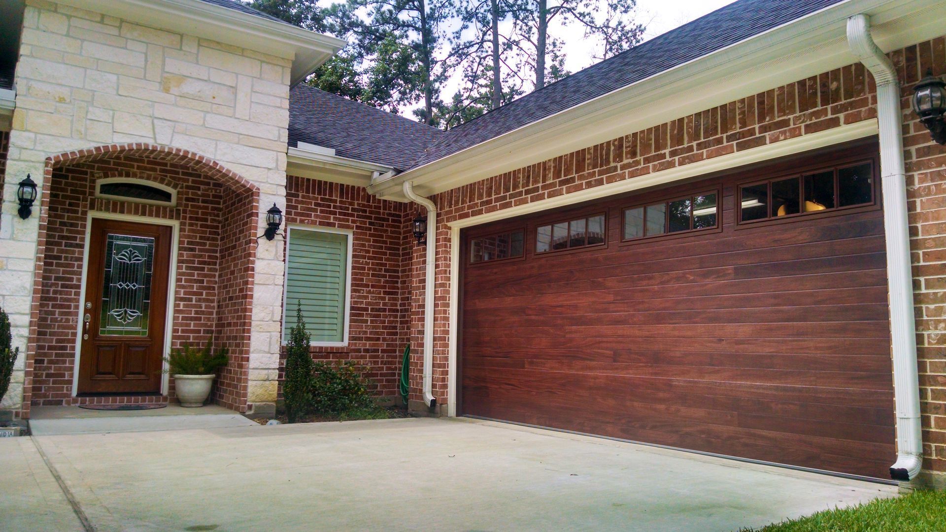 A house exterior with a wooden garage door, brick and stone siding, and a wooden front door with a glass inlay.