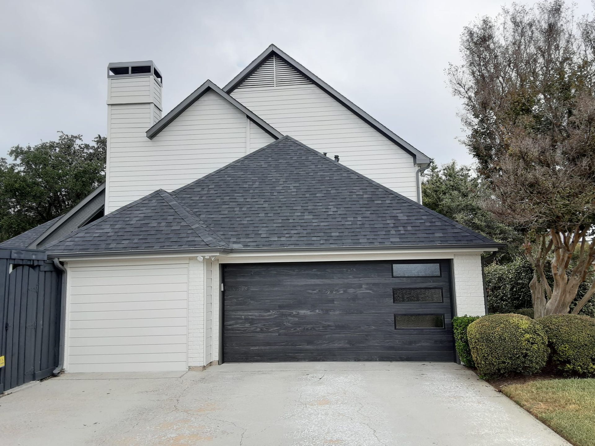A two-story white house with a charcoal-colored garage door and matching roof under a cloudy sky.
