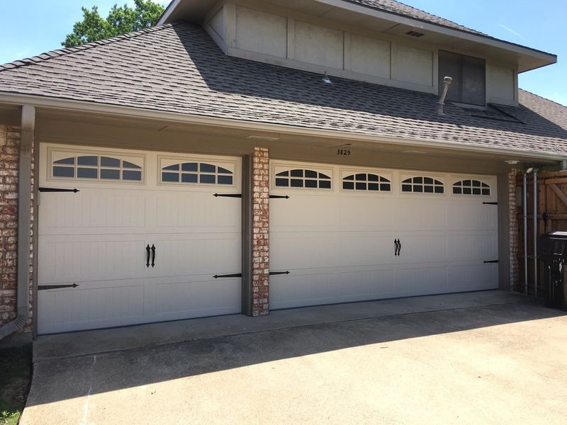 A white, three-car garage with arched windows, decorative black hinges, and brick pillars on a suburban home.