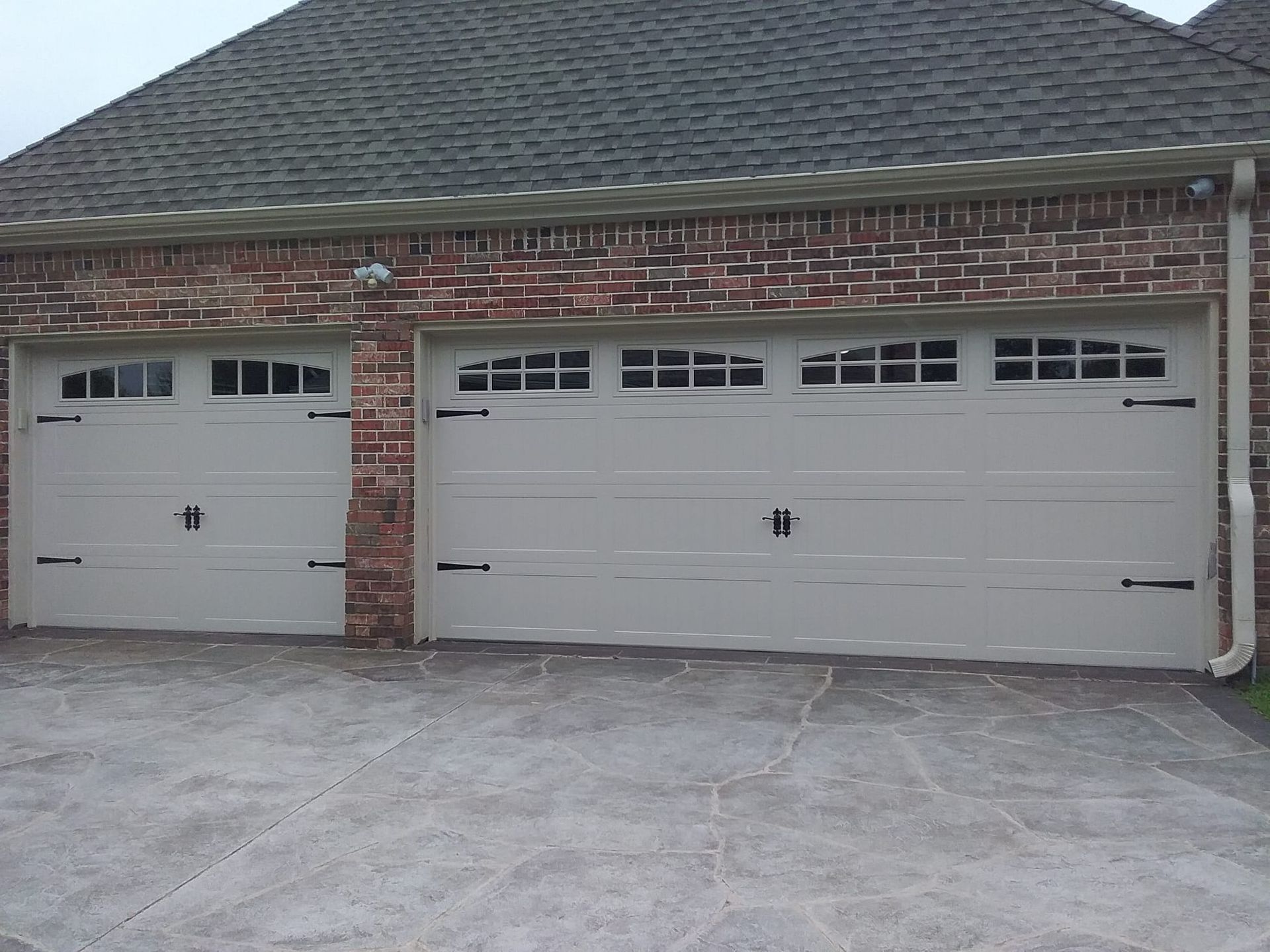 A brick-fronted garage with a double-bay door and a single-bay door, both cream-colored with decorative window panes.