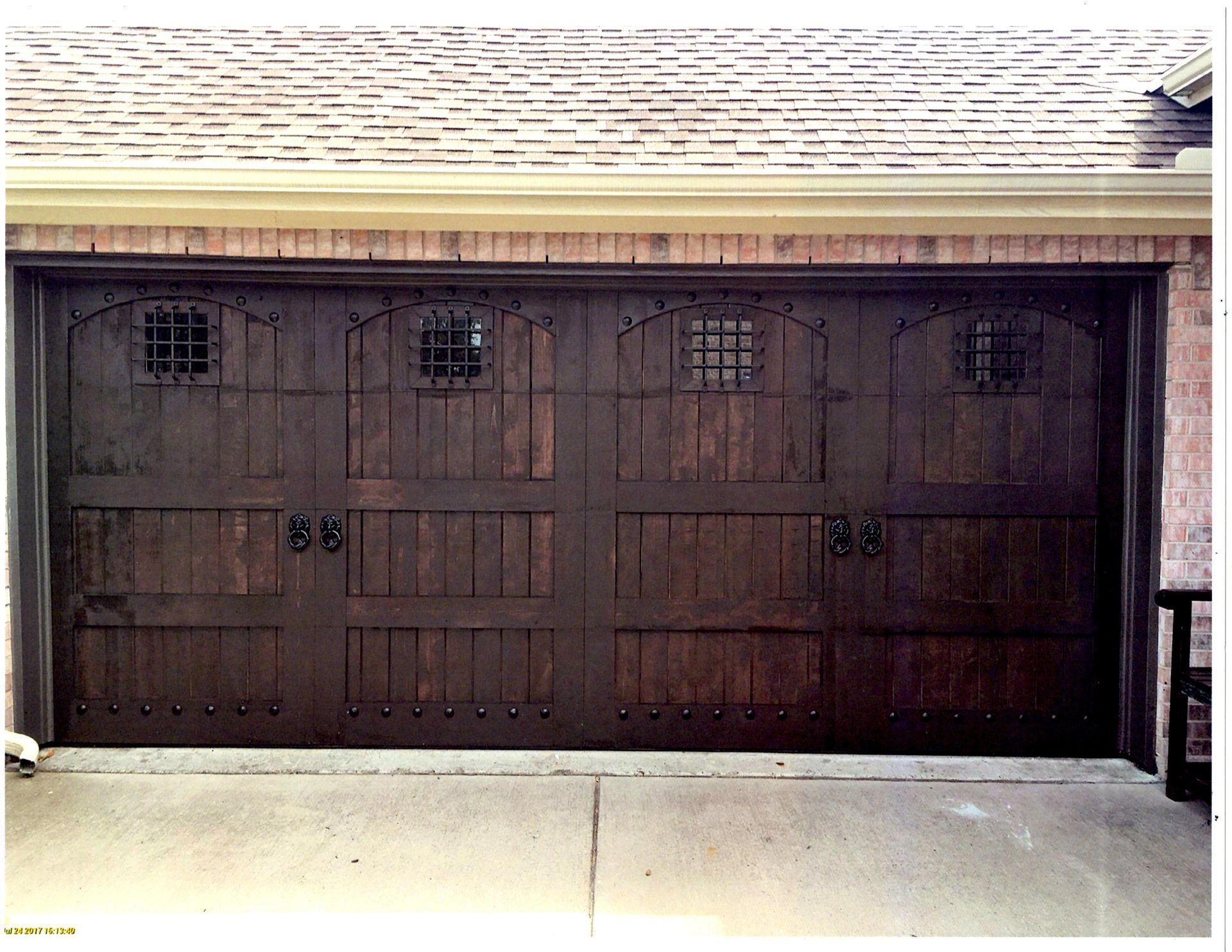 A dark wood garage door with four arched windows featuring metal grates, decorative studs, and iron handles.