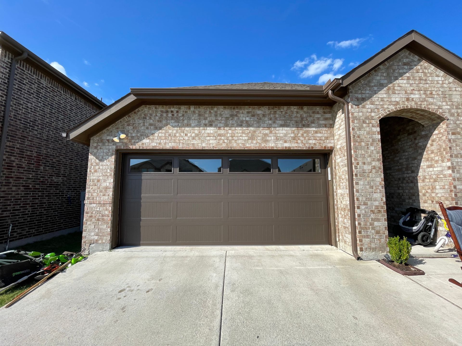 A single-story brick house with a brown two-car garage door and a concrete driveway under a clear blue sky.