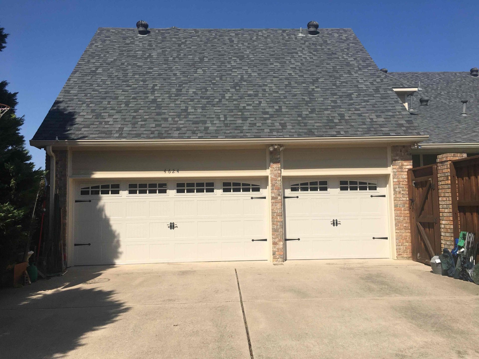 A two-car garage with white doors, brick trim, and a gray shingled roof under a clear blue sky.