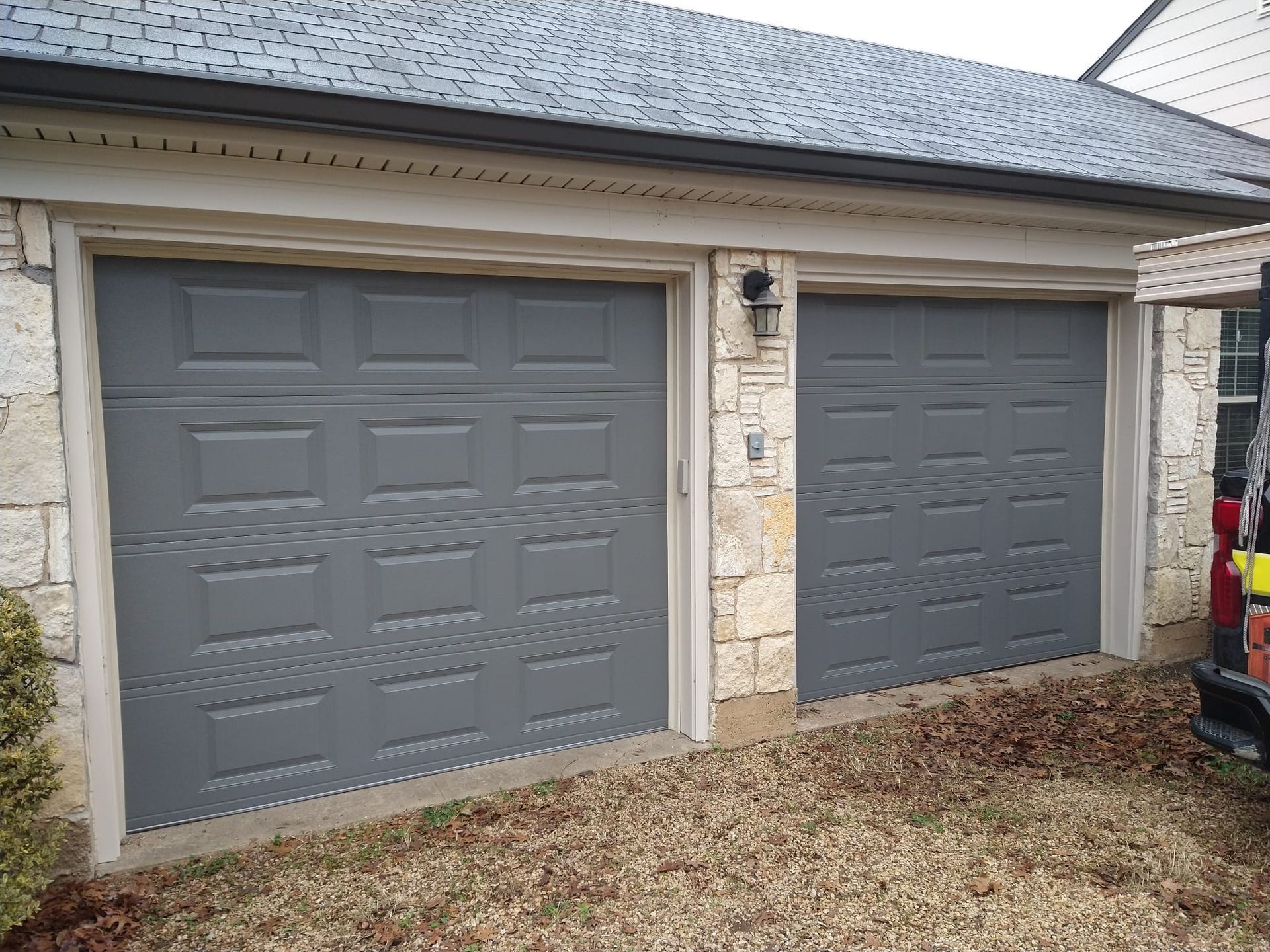 A two-car garage with gray sectional doors on a house with stone siding.