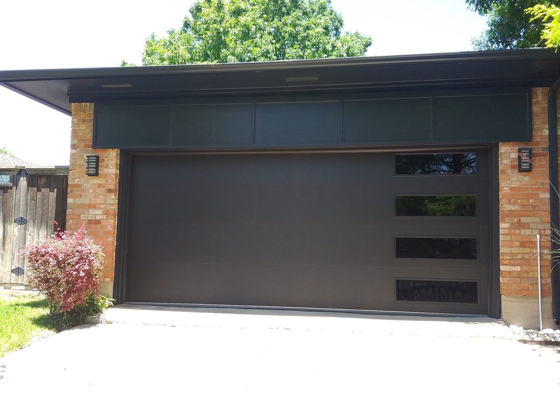 A modern brown garage door with a column of four narrow horizontal windows on the right, set in a brick exterior.