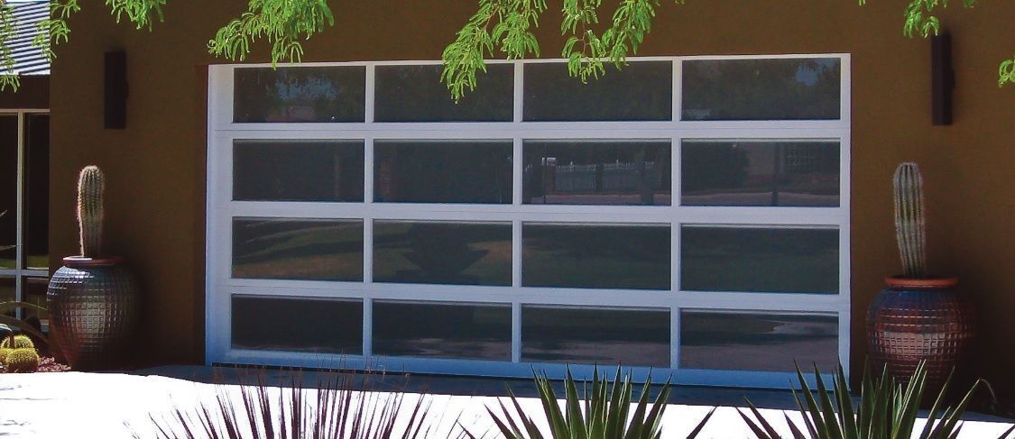Modern garage door with white frame and frosted glass panels, flanked by large potted cacti against a brown stucco wall.