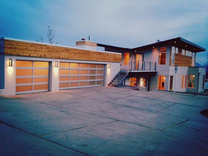 A modern two-story home with a two-car glass garage, concrete driveway, and natural wood accents at dusk.