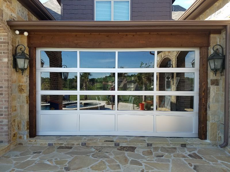 A modern white-framed garage door with glass panels set in a stone exterior house wall under a wooden beam.