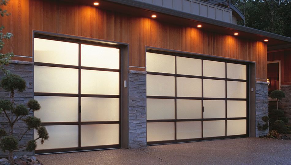 Modern two-car garage with frosted glass panel doors, stone accents, and wood siding under recessed outdoor lighting.