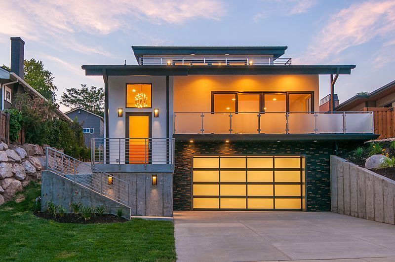 A modern two-story home at dusk with a lit garage, balcony, and front entrance, set on a landscaped lot.