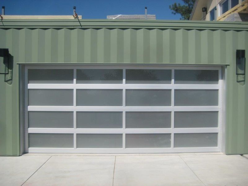 A modern, white-framed garage door with horizontal frosted glass panels set into a green, corrugated container-style wall.