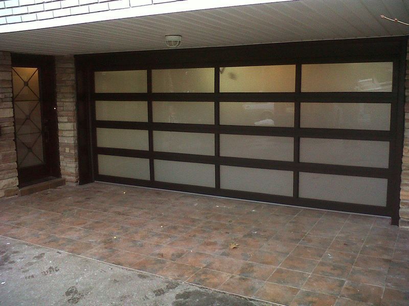 Modern garage with dark brown frame and frosted glass panels next to a matching glass-paned front door on a tiled patio.