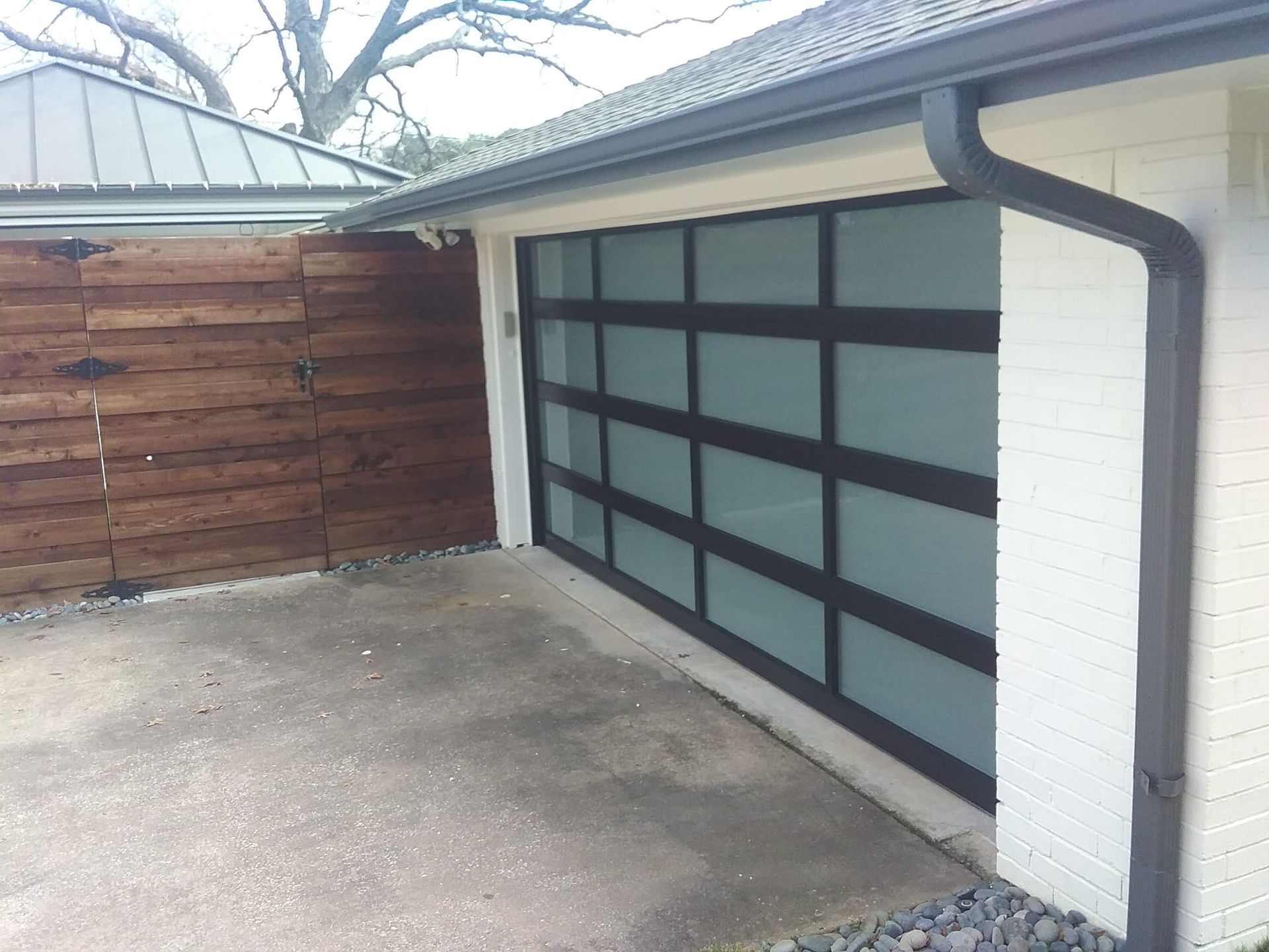 Modern garage door with frosted glass panels and black framing next to a wooden fence and white brick wall.
