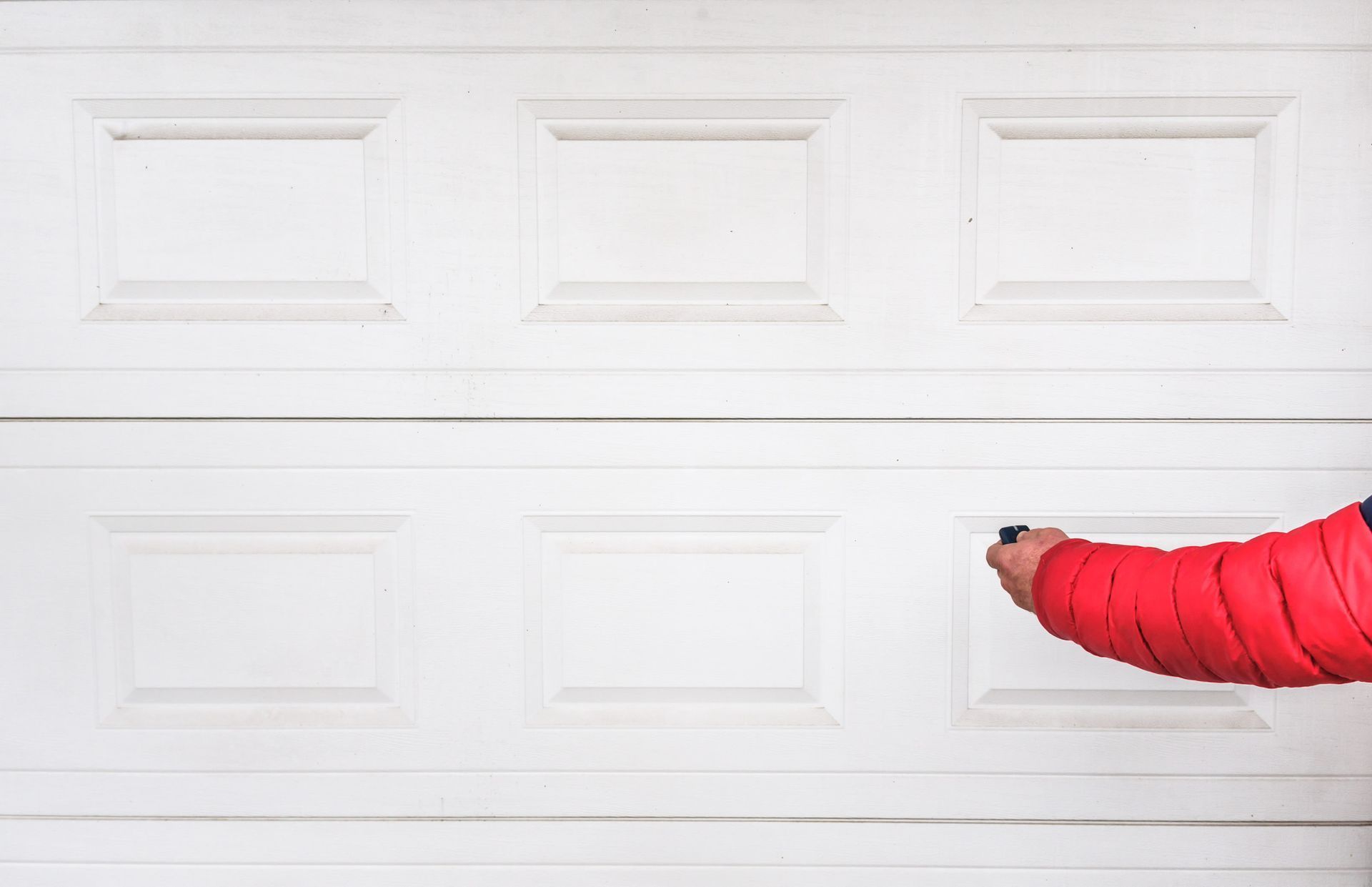 Hand in red sleeve using remote to open a white garage door.