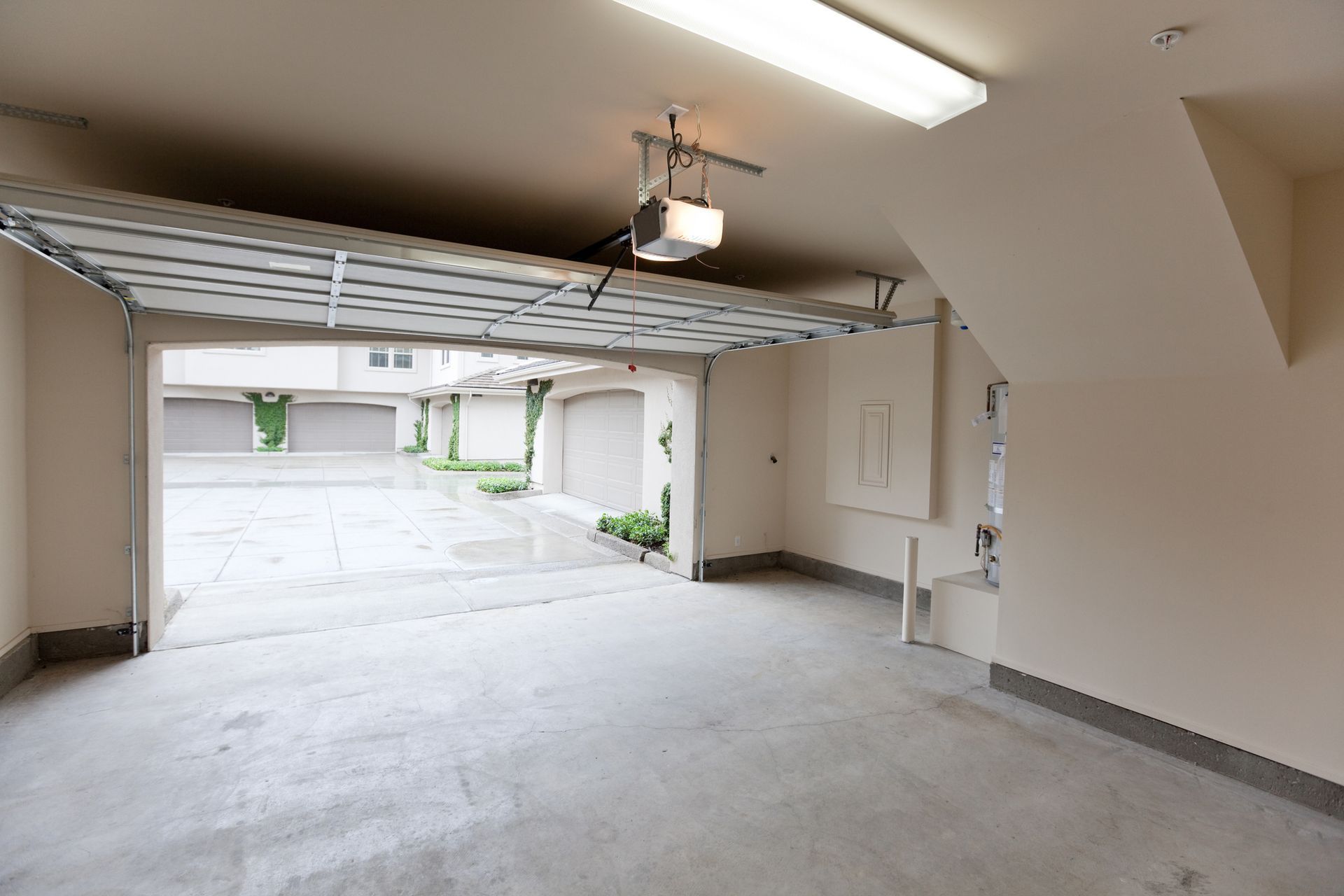 Empty, open garage; concrete floor, white walls, and view of townhouses outside.