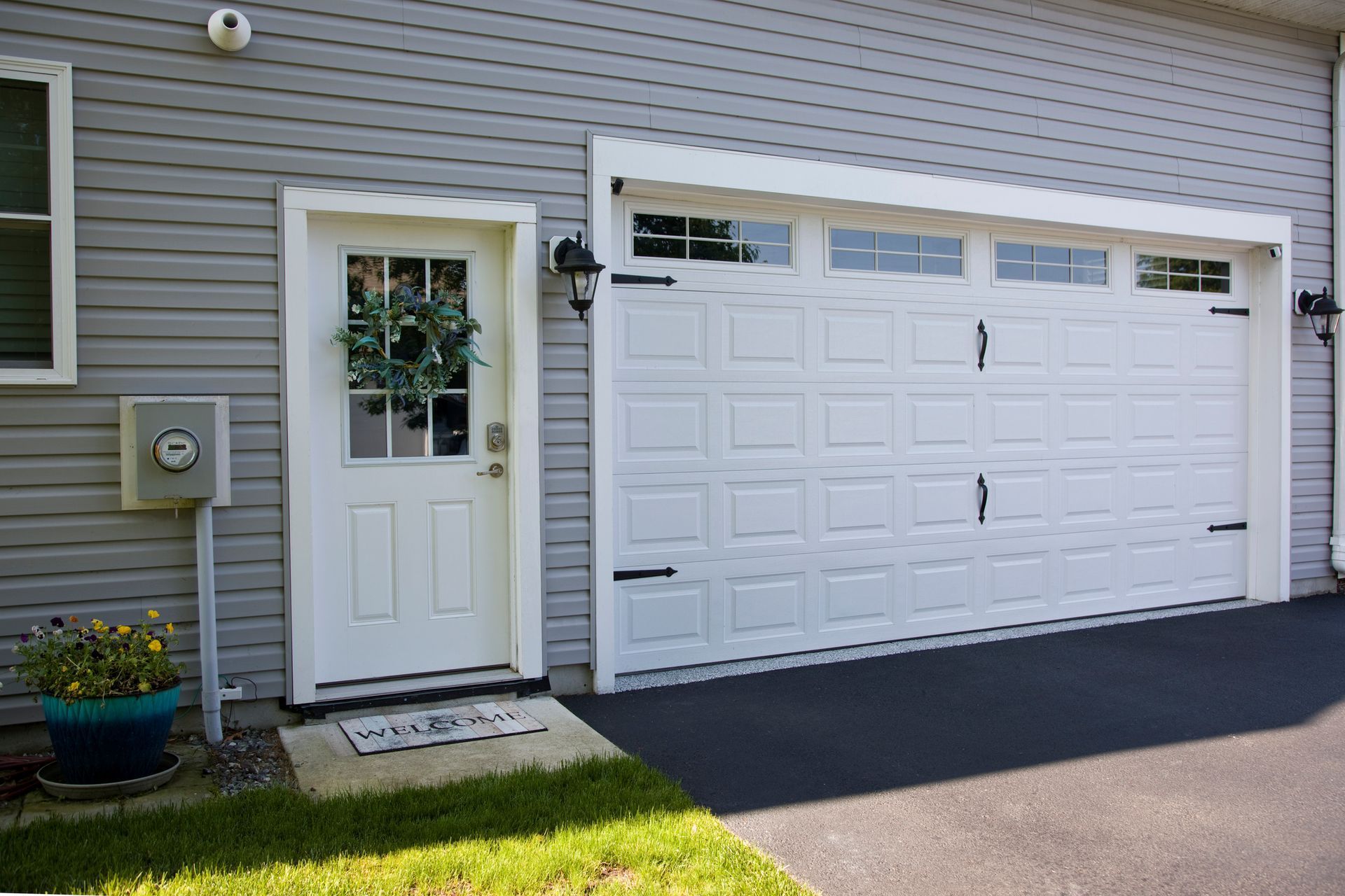 White garage door and matching door next to light gray siding. Green wreath on the front door.