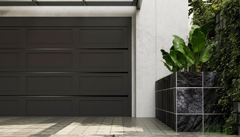 Black garage door next to a square stone planter with green plants and ivy.