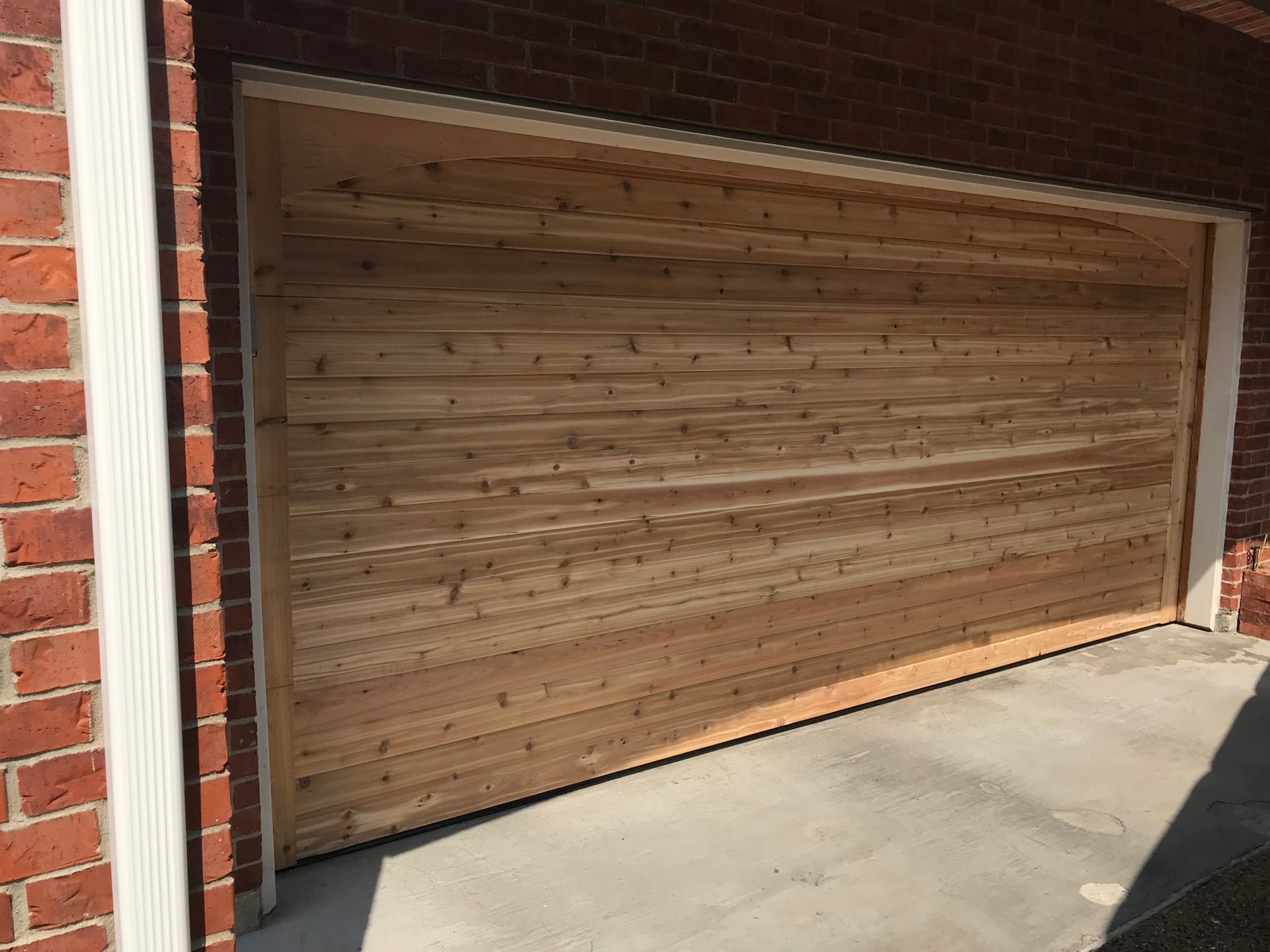 A garage door covered in horizontal natural wood planks, set into a red brick house wall.