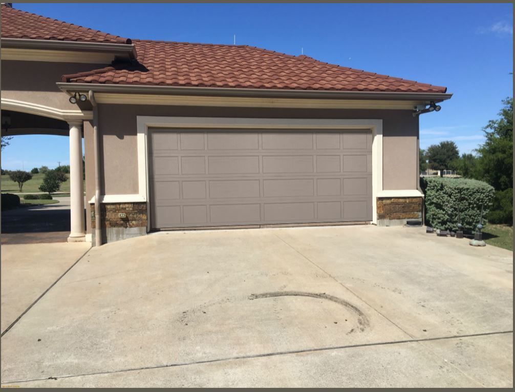 A beige two-car garage with a brown tiled roof and stone accents, set against a clear blue sky.