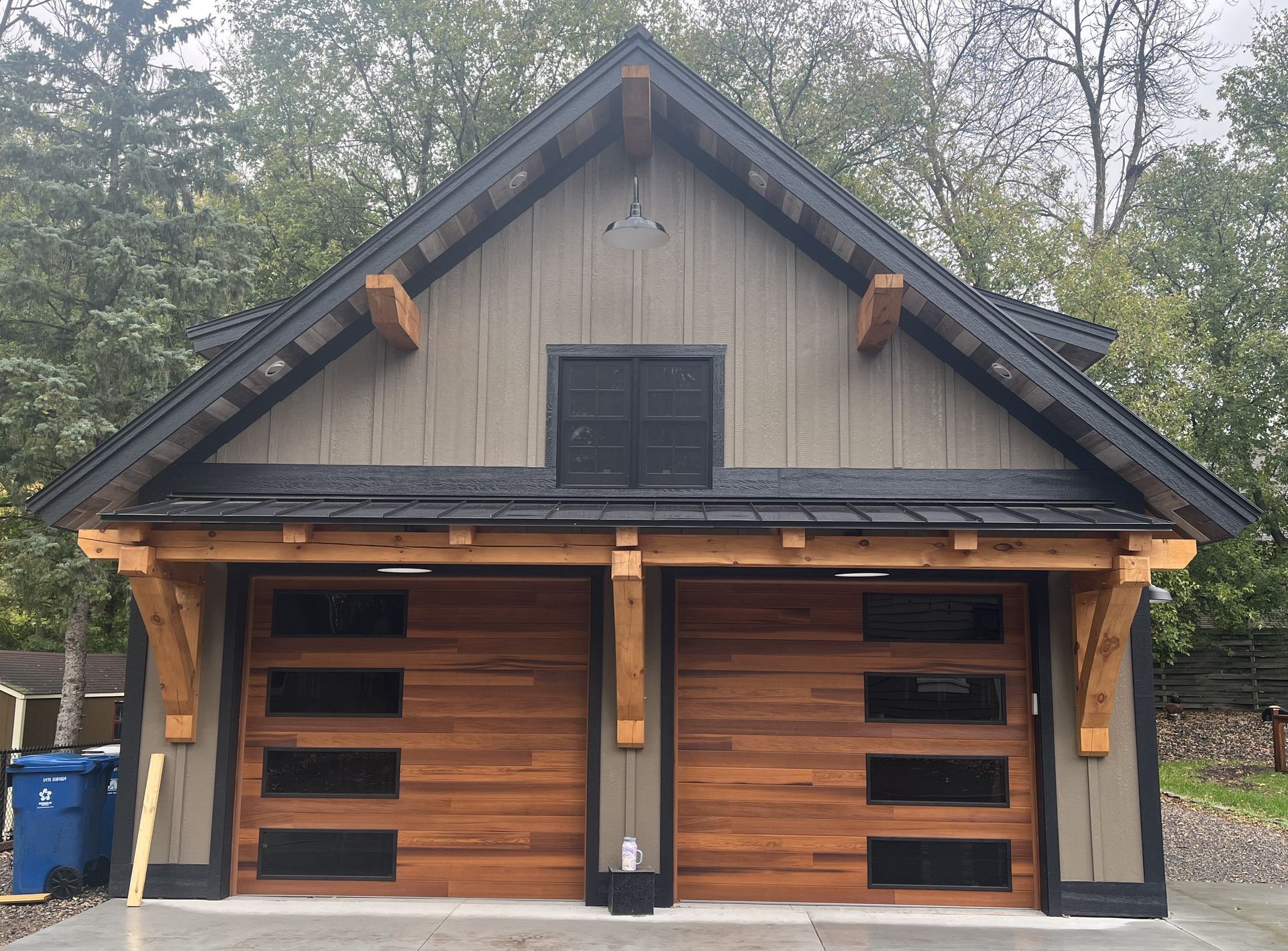 A rustic, wood-and-stucco two-car garage with modern dark-trimmed wooden garage doors and heavy timber supports.