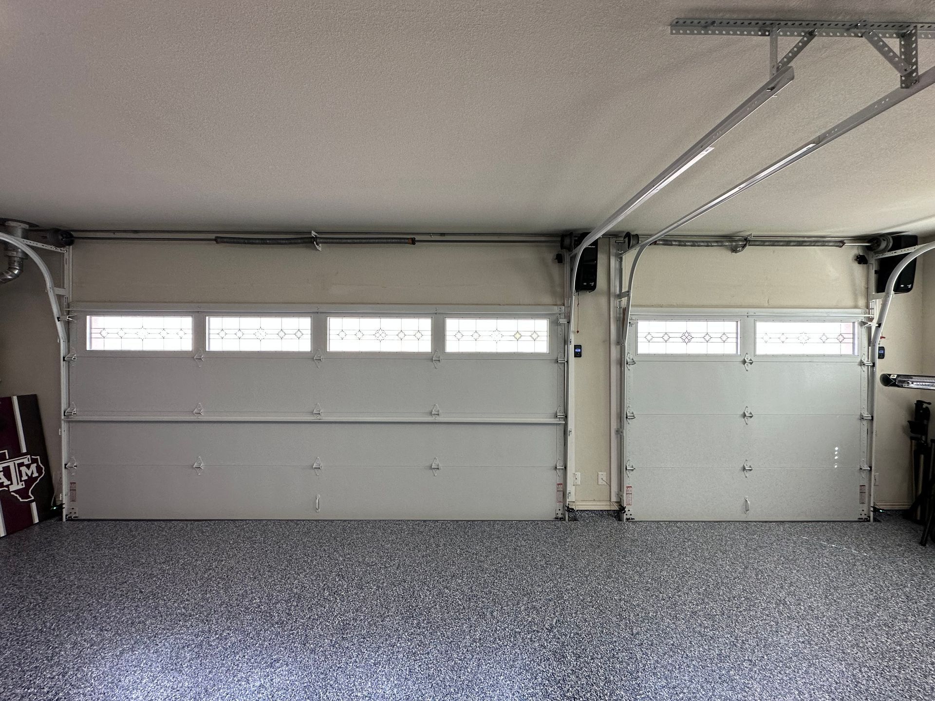 Two closed white garage doors, with windows at the top, inside a garage with speckled flooring.
