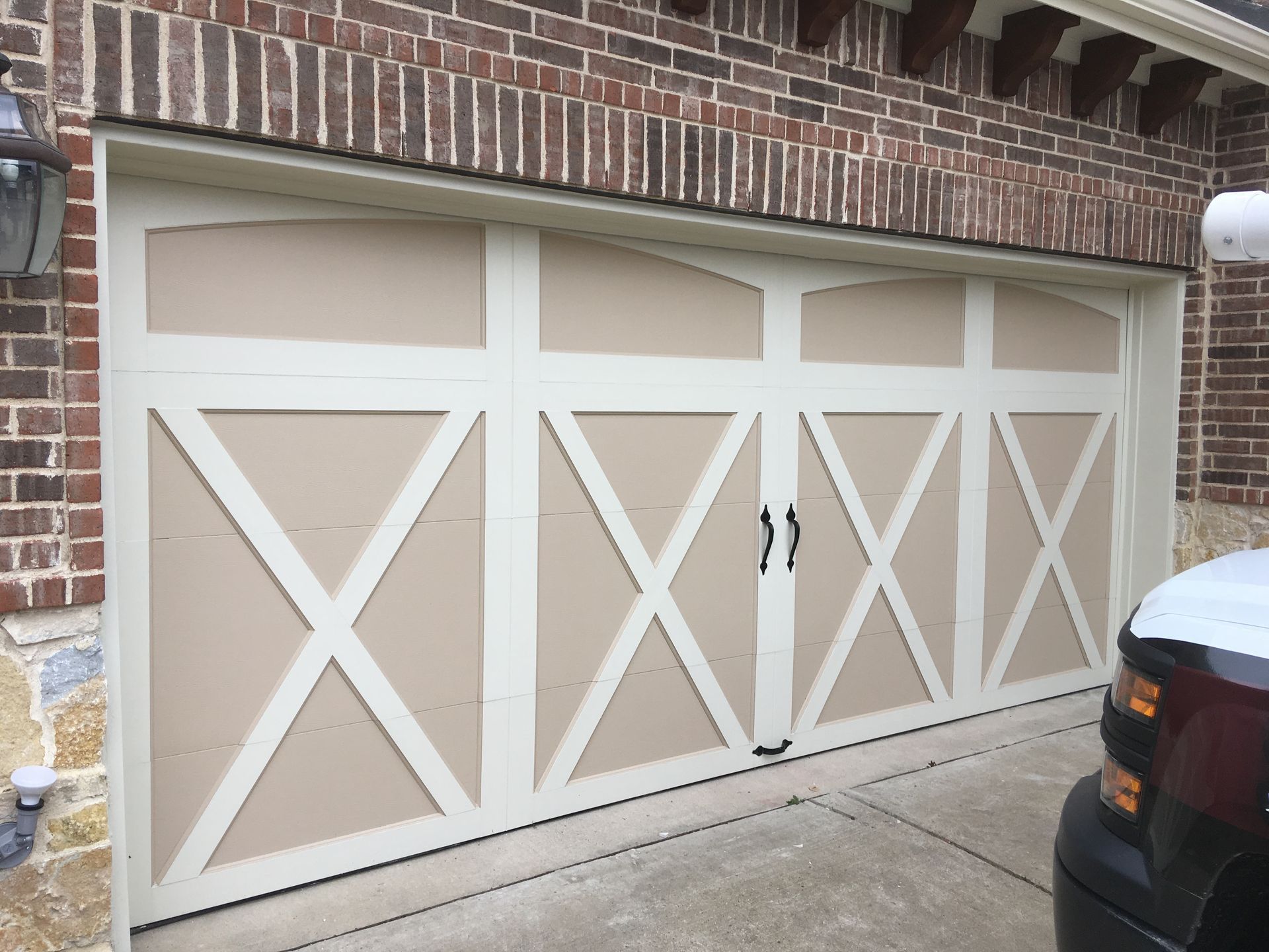 A beige residential garage door with white trim and a decorative