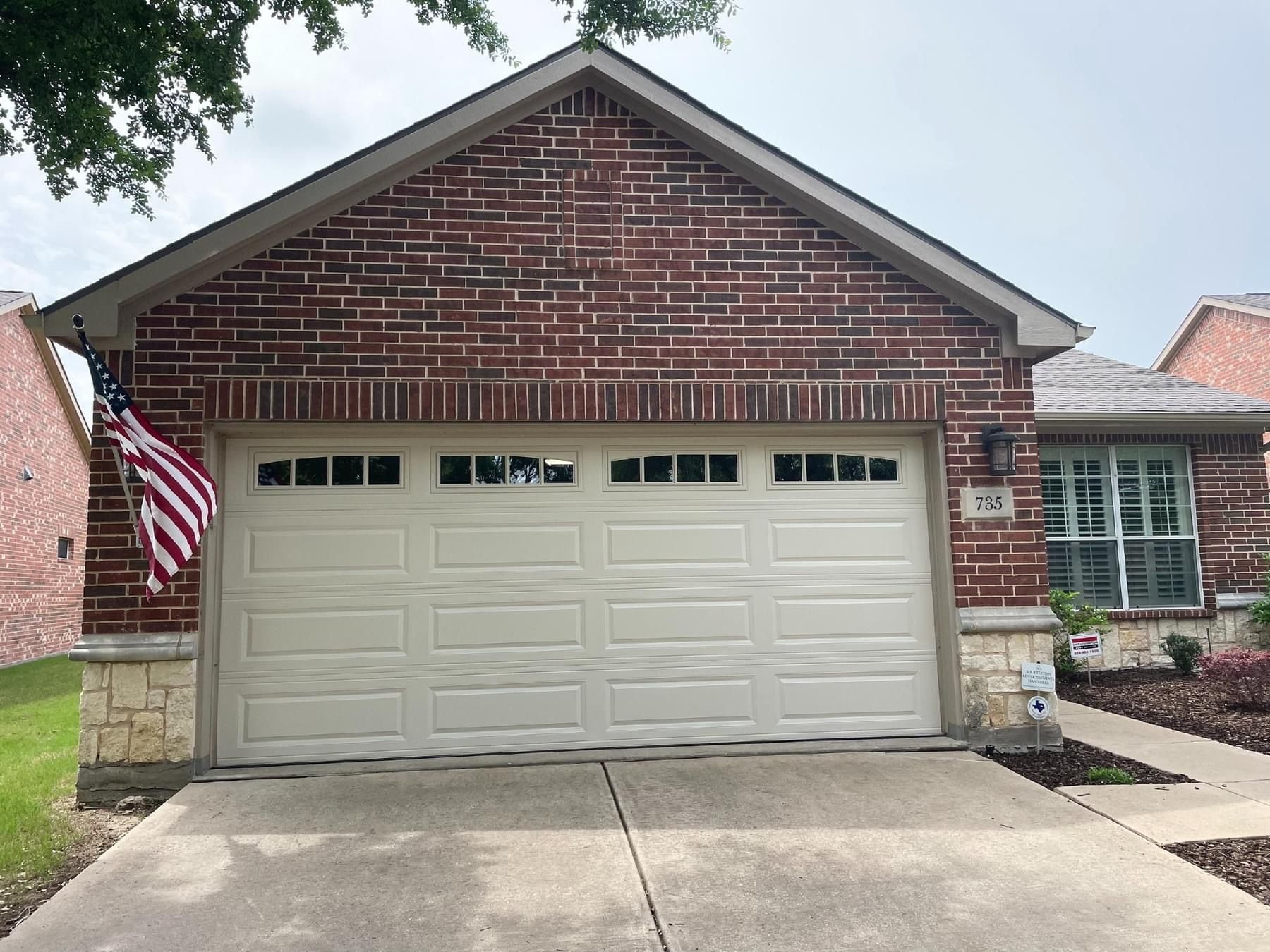 A single-story suburban home with red brick, beige stone accents, and a beige two-car garage with small windows.