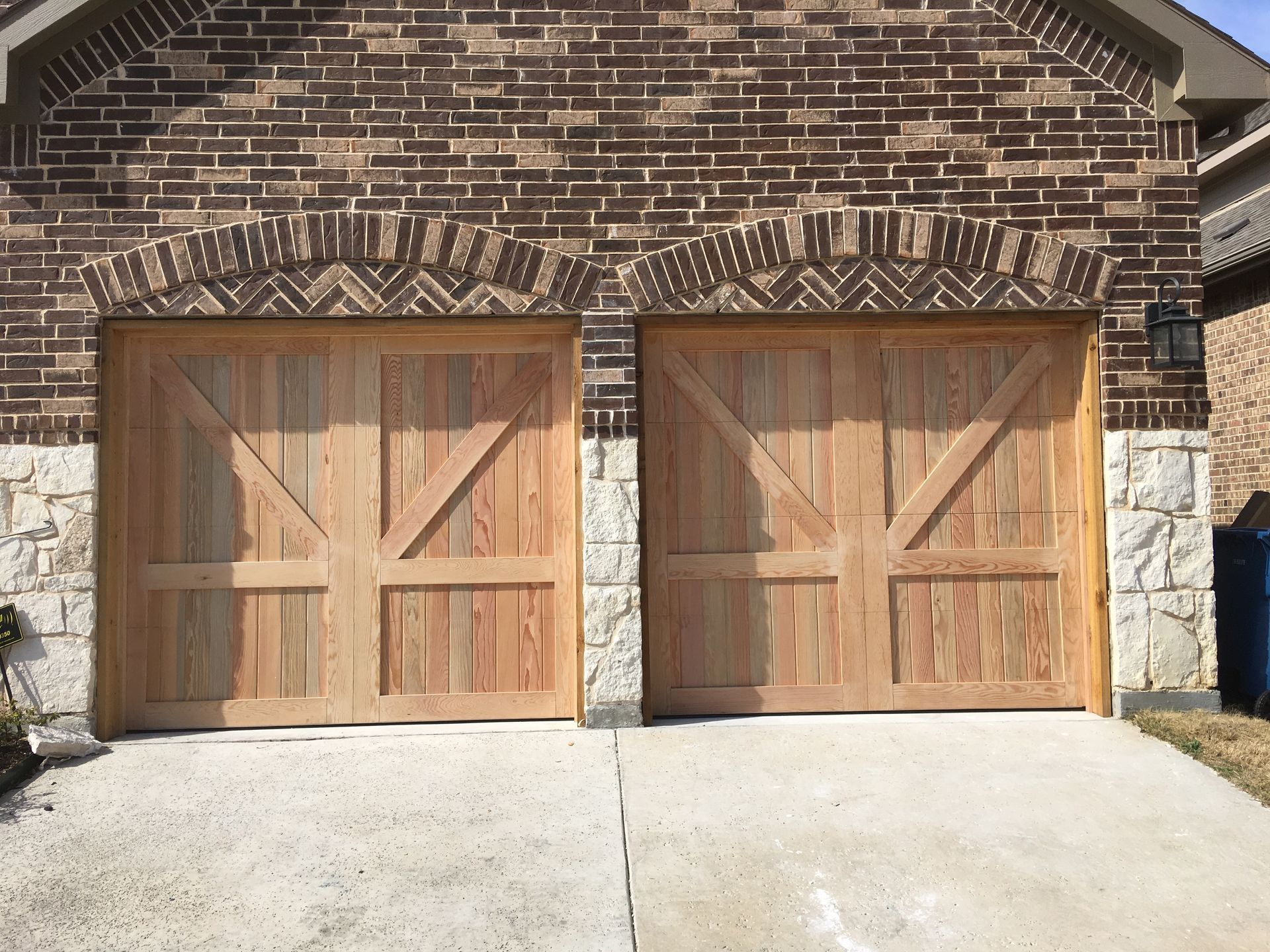 Two wooden garage doors with diagonal bracing under brick arches, set in a stone and brick exterior wall.