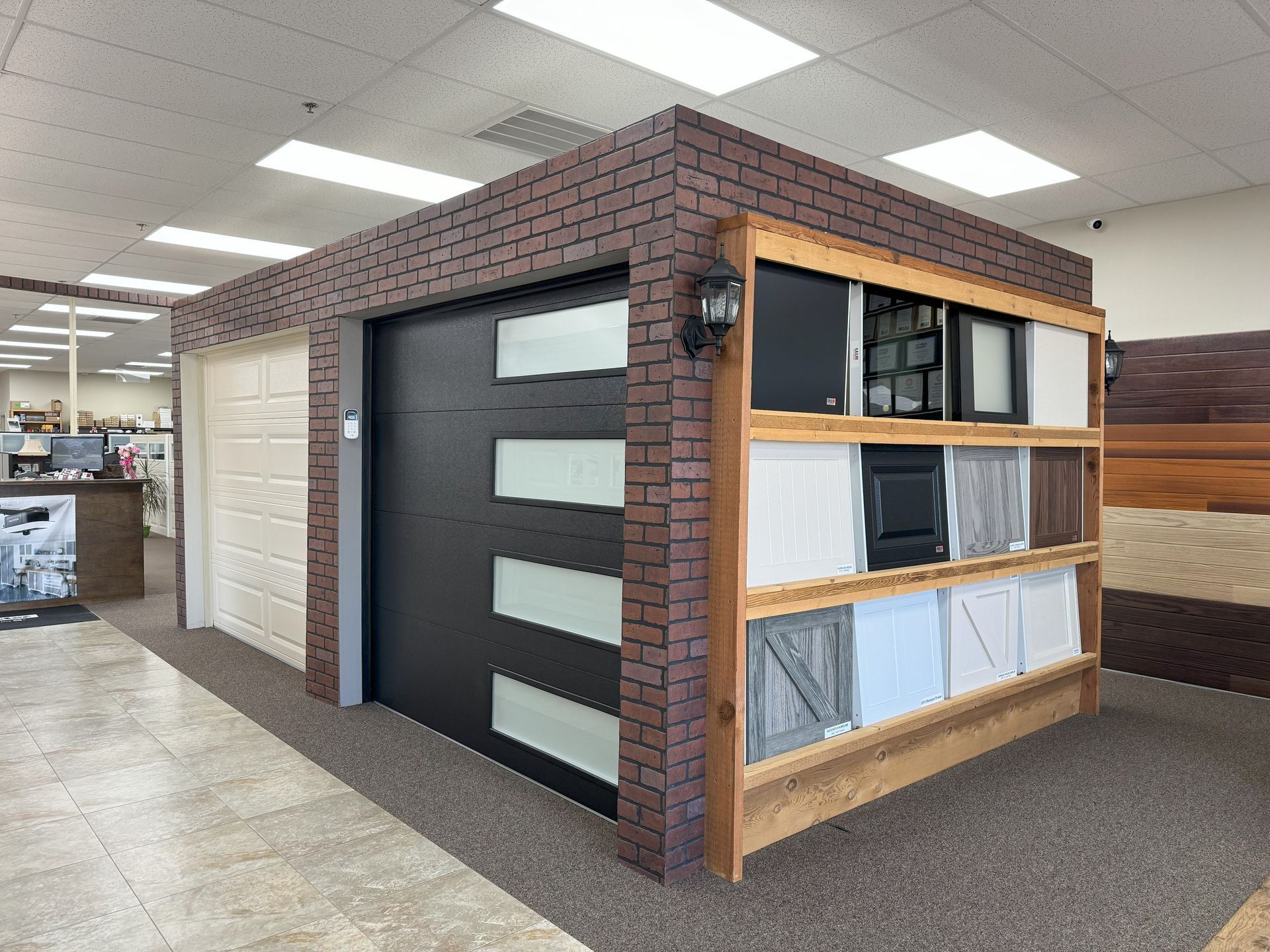 Garage door display in a showroom, featuring door styles and color samples. Brick facade with neutral flooring.