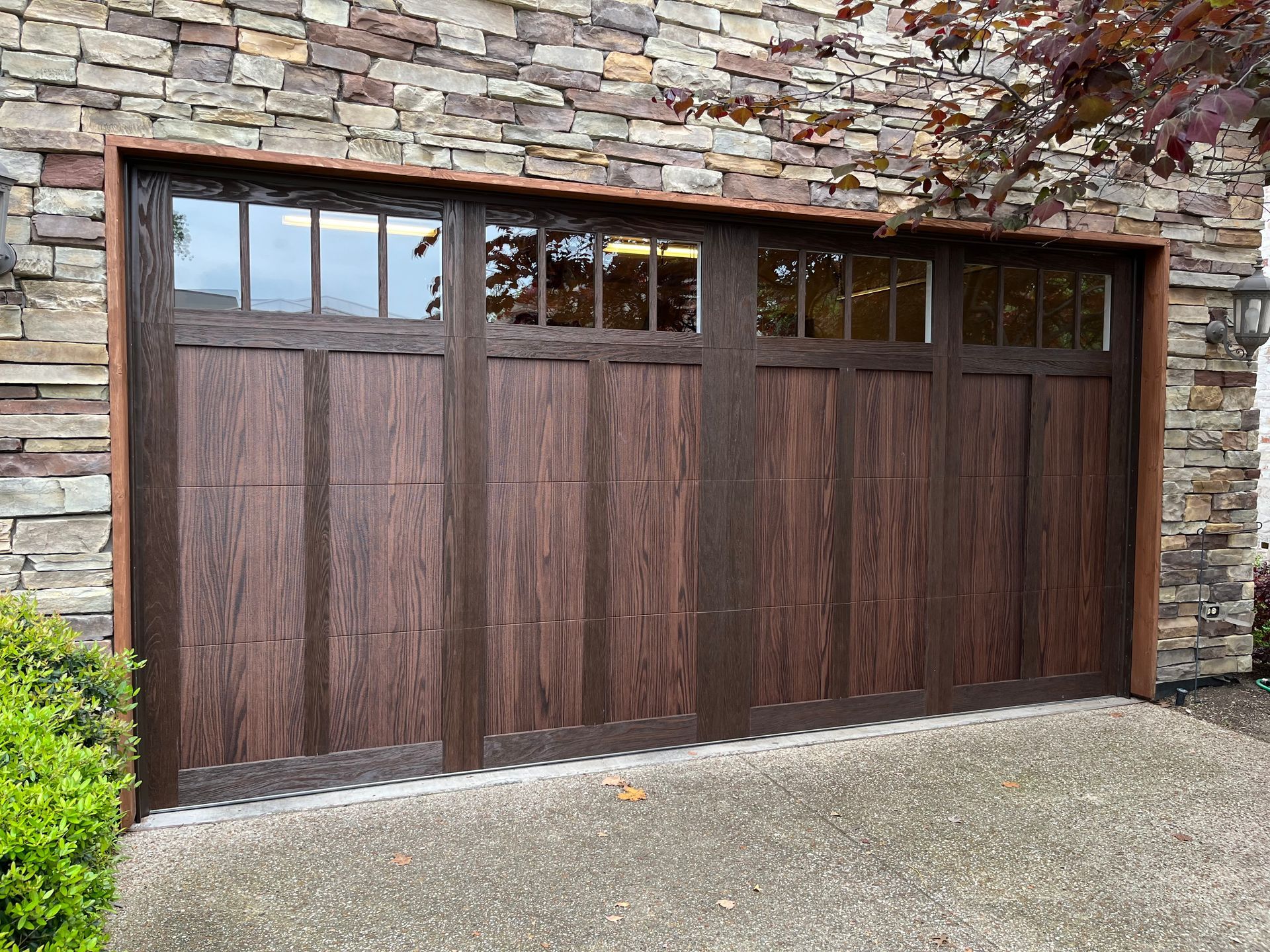 Brown faux-wood garage door with glass panels set in a stone wall facade.