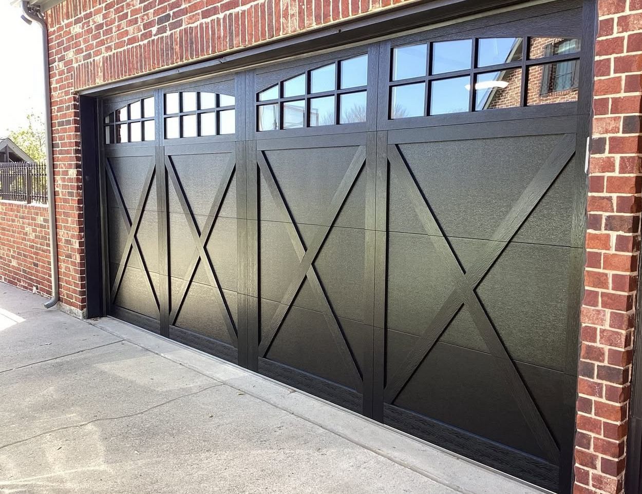 Black carriage-style garage door with X-pattern trim and glass window panes on a red brick house.