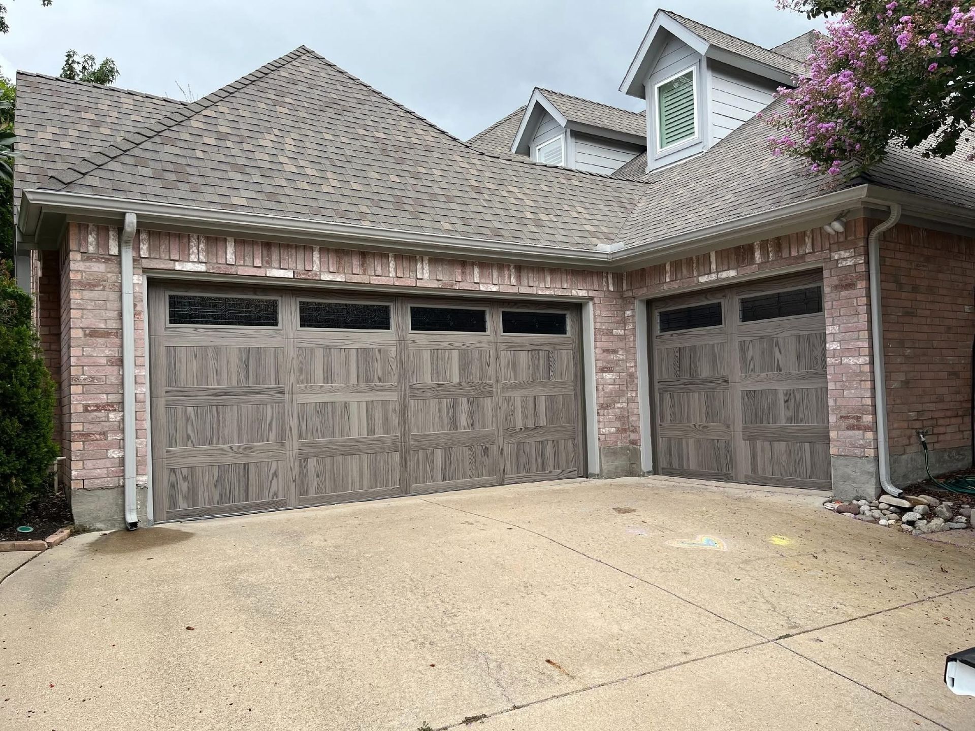 A brick house exterior featuring a three-car garage with wood-style doors and a textured shingle roof.
