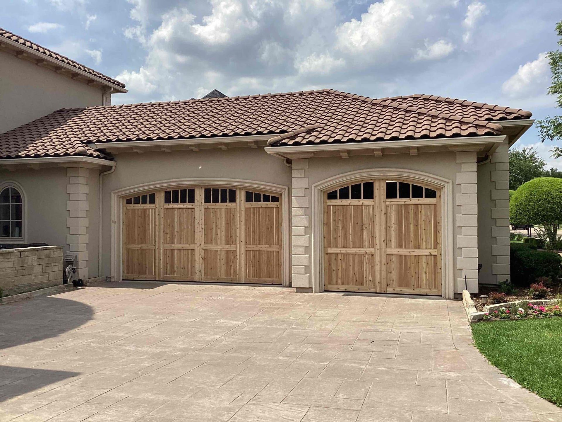 A stucco house with a tiled roof featuring a triple garage door and a single garage door, both made of light wood.